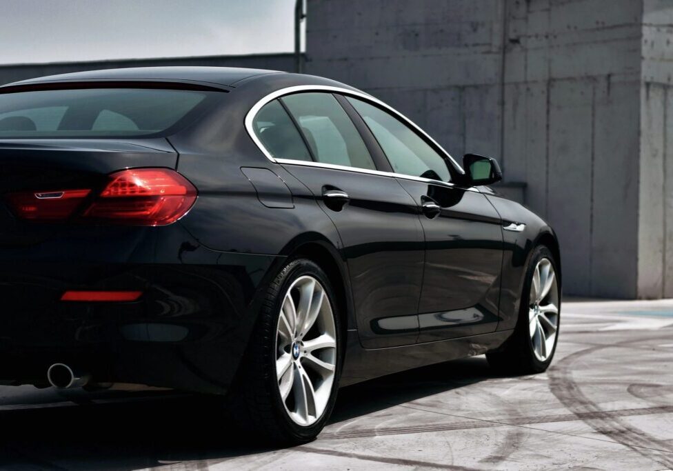 A black car parked in the street near a wall.